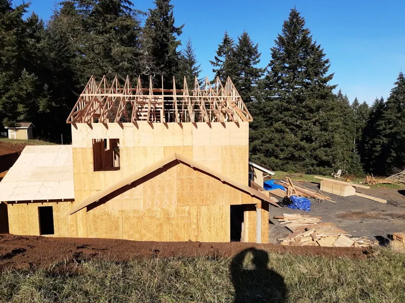 OSB-sheathed two-story ADU framing with roof trusses being set on an Oregon hillside property by Red Umbrella Contractors.