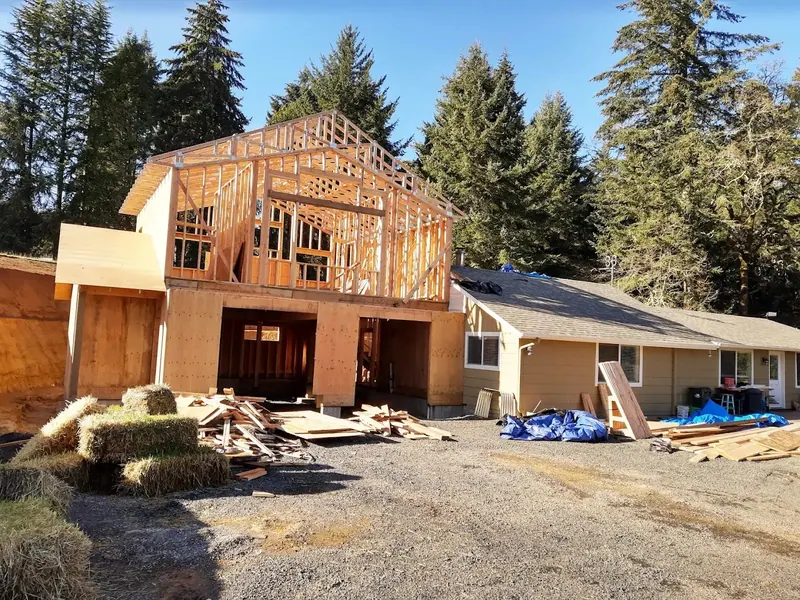 In-progress framing of a two-story home addition attached to an existing ranch house, showcasing Red Umbrella's structural expertise in Eugene, Oregon.