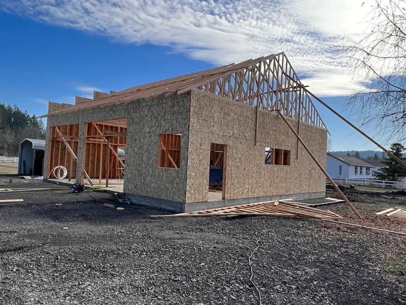 New detached garage under construction showing OSB wall sheathing and roof trusses set on a rural property, a Red Umbrella garage build project.
