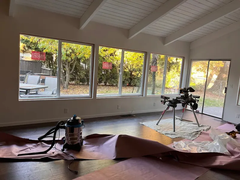 Interior of a vaulted room addition near completion, showing white shiplap ceiling, exposed beams, and a new sliding glass door, by Red Umbrella.