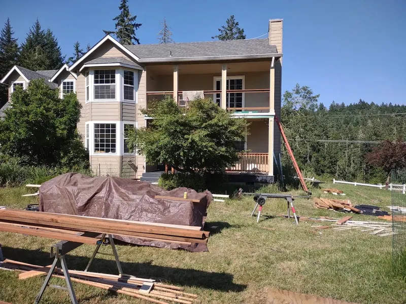 A two-story craftsman home with a bay window and covered upper porch during outdoor deck construction by Red Umbrella.