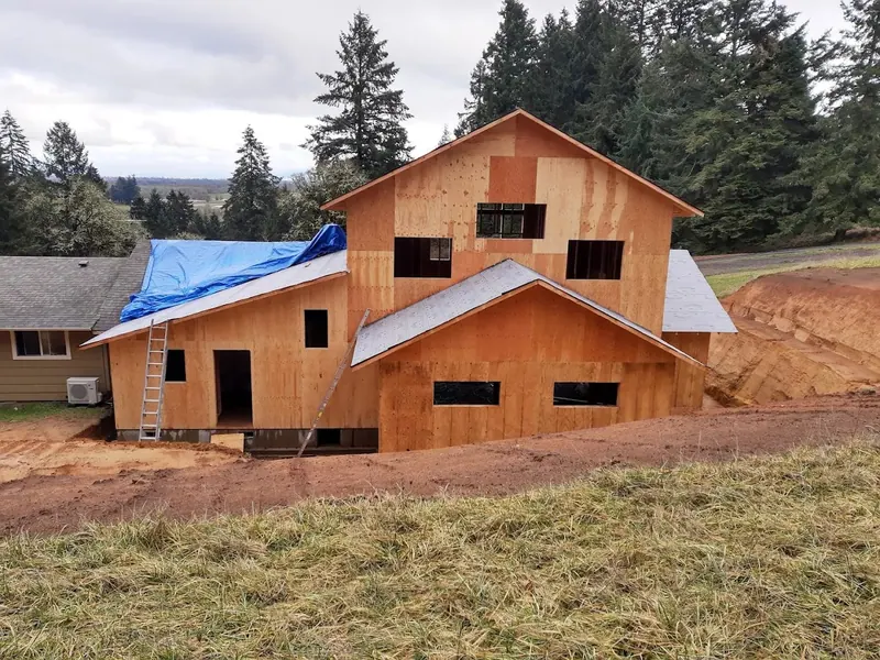 Two-story home addition with OSB sheathing and tarped roof under construction on a rural hillside property in the Eugene Oregon area by Red Umbrella.