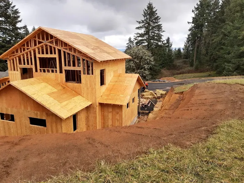 A large two-story home addition under construction on a hillside lot surrounded by Douglas fir trees in the Eugene Oregon region, Red Umbrella.