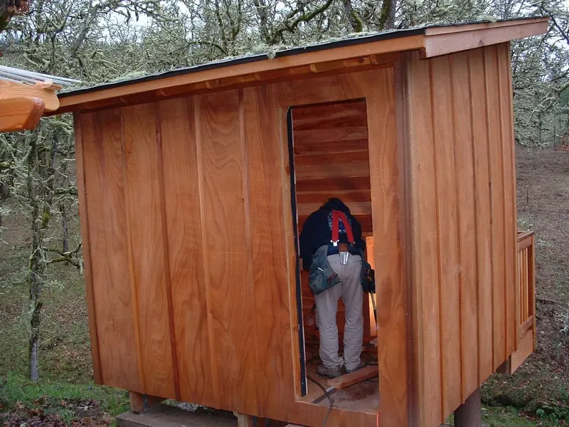 A small outbuilding or shop being finished with vertical cedar siding and a lean-to roof, built by Red Umbrella in a rural Oregon oak woodland setting.