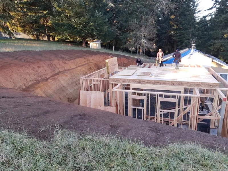 Aerial view of workers setting second-floor framing and OSB subfloor on a hillside home addition in the Eugene Oregon area, Red Umbrella.