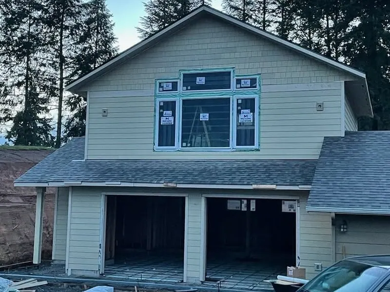A two-story garage addition with olive-tan lap siding and new windows being installed on a wooded property near Eugene Oregon, Red Umbrella.