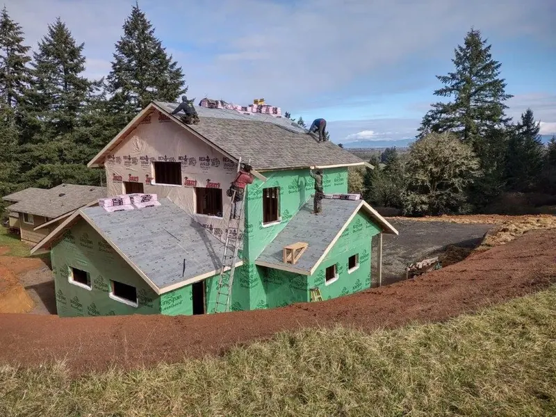 A roofing crew lays asphalt shingles over rigid insulation board on a large two-story home addition under construction on a hillside site in Eugene Oregon, Red Umbrella.