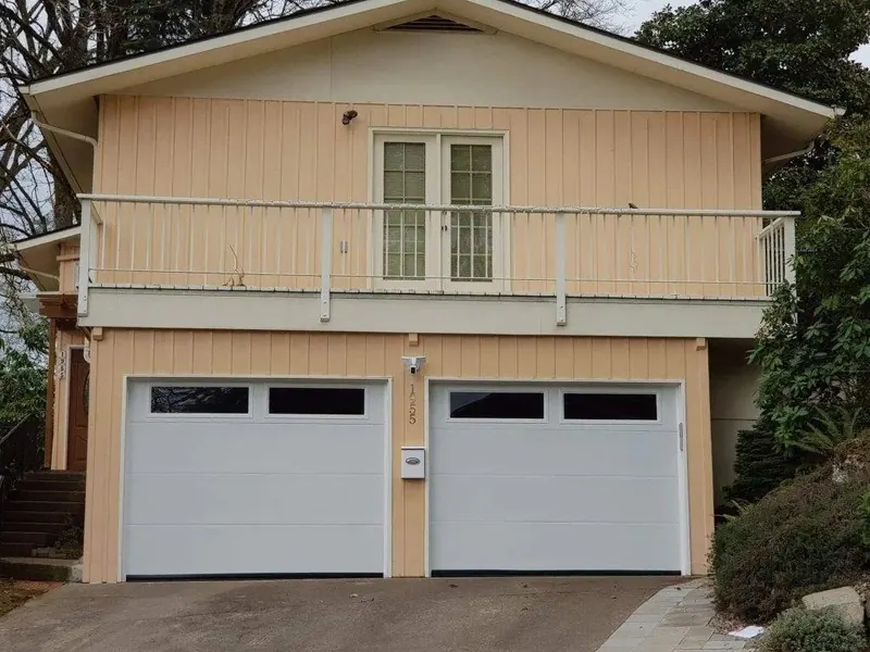A two-car garage with a full second-story ADU unit and wide balcony, finished in cream board-and-batten siding, built by Red Umbrella in Eugene Oregon.