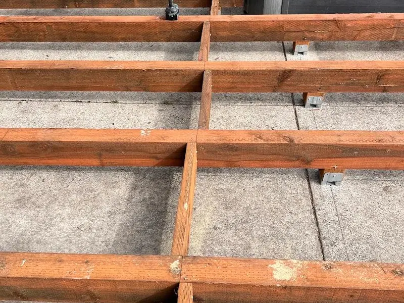 Pressure-treated deck joist framing installed over a concrete pad with galvanized post bases during a Red Umbrella deck build.