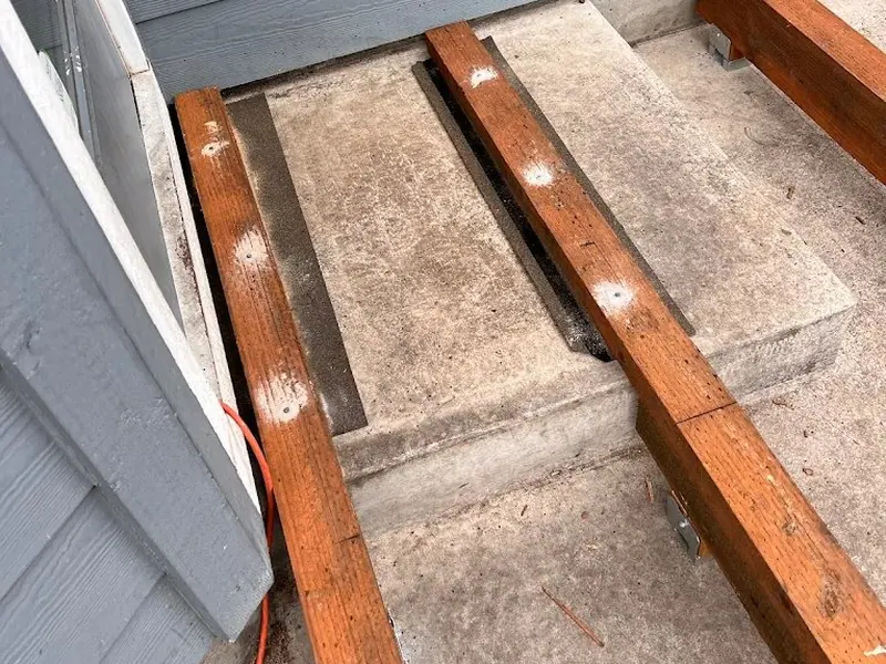 Close-up of pressure-treated deck ledger and joist framing being attached to a home with blue-grey siding on a Red Umbrella deck project.