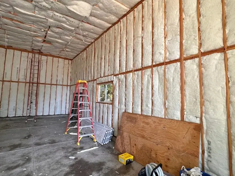 Garage interior with spray-batt insulation filling orange metal stud framing on walls and ceiling, a Red Umbrella garage build in progress.