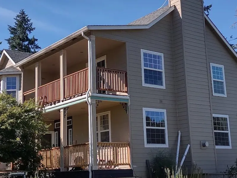 Two-story home addition with stacked wraparound porches and new wood railings nearing completion on a Red Umbrella home addition project.