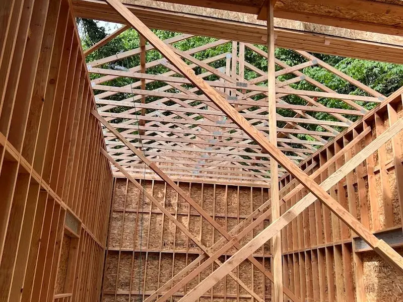 Interior view of garage framing from the ground looking up, showing complex roof rafters and wall bracing during construction.