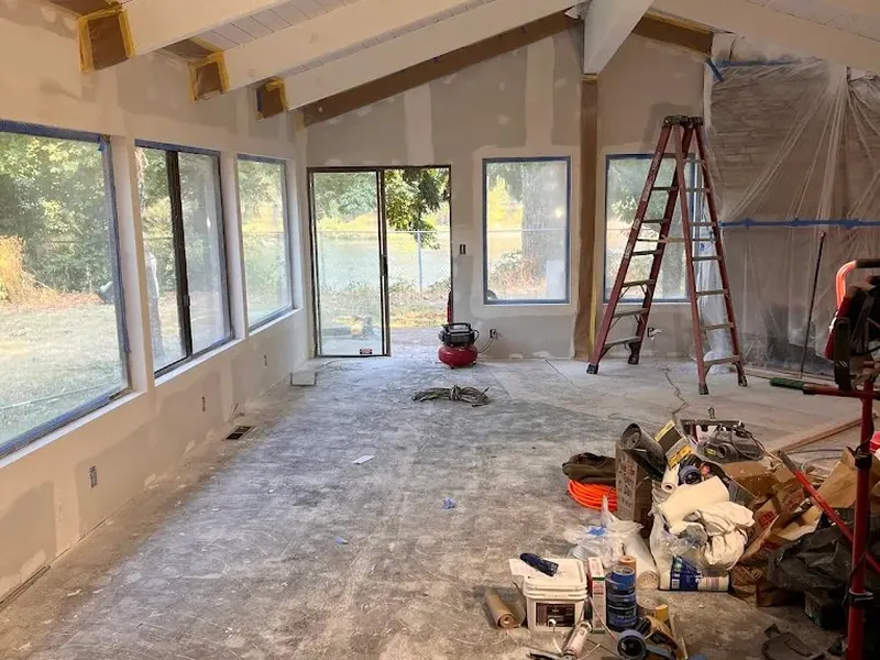 Renovated living room with new drywall, freshly installed large windows, and vaulted beam ceiling ready for flooring by Red Umbrella.