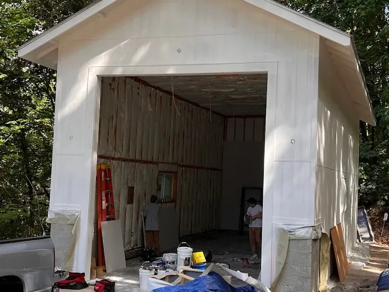 Detached garage with fresh white exterior paint and spray foam insulation visible inside the open bay during finishing by Red Umbrella.