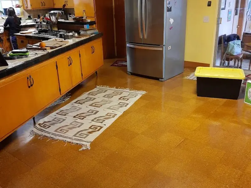 Dated kitchen with honey oak cabinets, orange linoleum tile floor, and stainless fridge — the before state of a Red Umbrella kitchen renovation project.