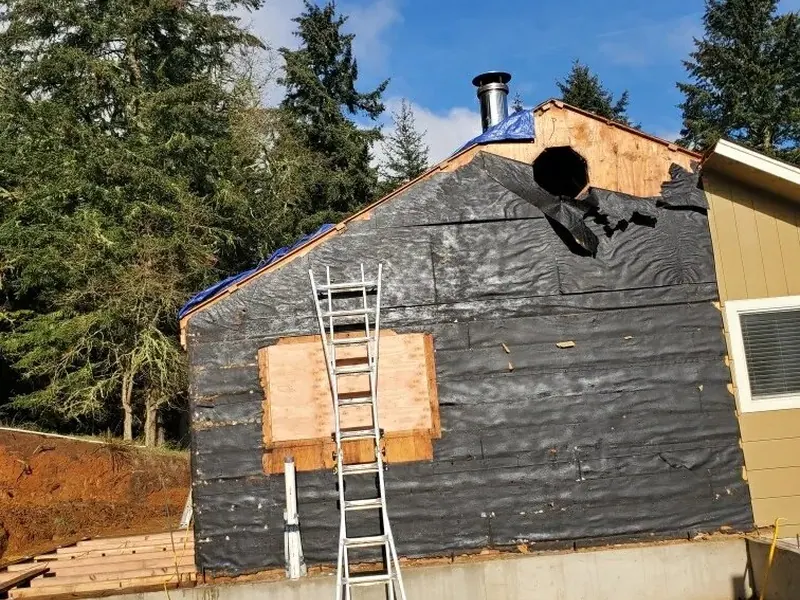 Gable end of a home stripped to housewrap with a round stovepipe cutout, mid-renovation by Red Umbrella in the Eugene, Oregon area.