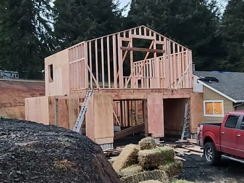 Framing stage of a two-story garage with ADU above, showing open gable and roof structure at dusk on a Red Umbrella job site near Eugene, Oregon.