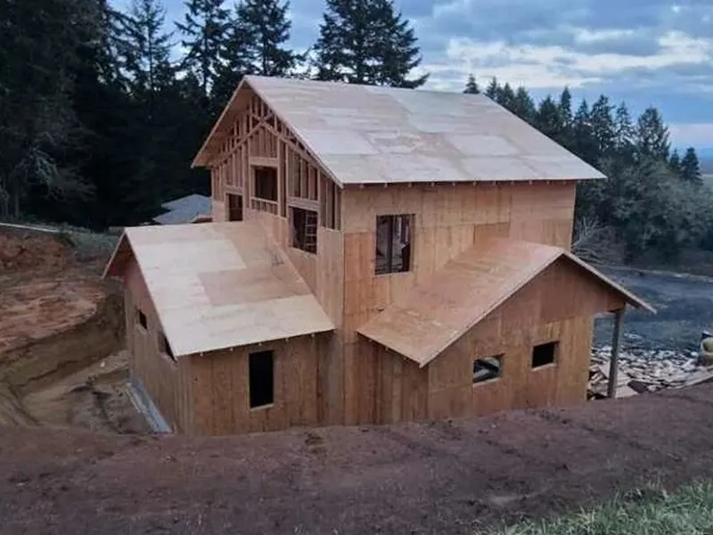 Two-story ADU fully framed and sheathed with OSB at twilight, showing Red Umbrella construction progress on a hillside site near Eugene, Oregon.